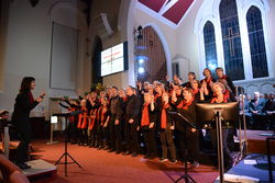 Noch reserviert im Hintergrund: Die Männer  Kendaler K Shoes Choir lauschen dem mitreißenden Auftritt des Gospelchors der Rintelner Johannis-Kirchengemeinde unter Dirigentin Kyra Rundfeldt in Kendals St. Thomas Church. Foto: tol